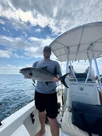 Angler proudly displaying a large fish while aboard a fishing boat in open waters.
