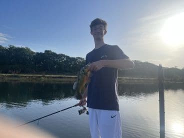 A young angler proudly displaying a catch of colorful bass while fishing in a serene freshwater environment.