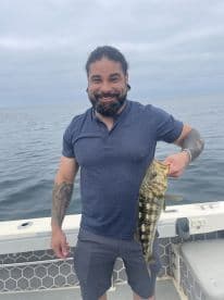 An angler proudly displaying a large Black Sea Bass while fishing on a boat in open waters.
