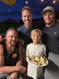A young boy proudly displaying a plate of freshly cooked fish with his family, celebrating a successful fishing trip.