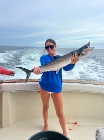 A young angler proudly displaying a large King Mackerel while fishing offshore, showcasing a successful day on the water.