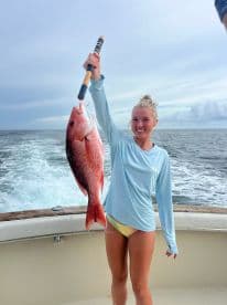A young angler proudly displaying a large Red Snapper while aboard a fishing boat, showcasing a successful day on the water.