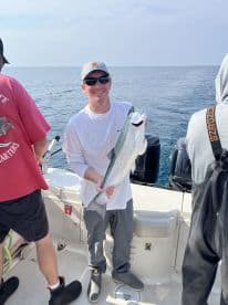 An angler proudly displaying a large Silver Salmon while fishing on a charter boat in open waters.