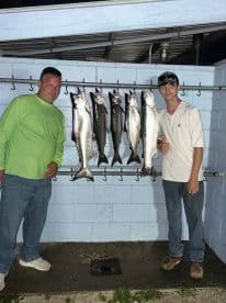 Two anglers proudly displaying their catch of several large fish on a catch board after a successful fishing trip.