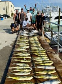 A group of anglers proudly posing with a large catch of Mahi Mahi displayed on a wooden board at the dock.