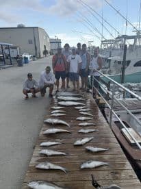 Group of anglers posing with a successful catch of multiple fish displayed on a dock after a fishing trip.