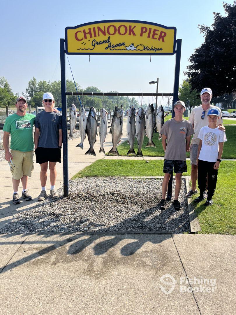 A family poses proudly in front of a catch board displaying several Chinook salmon at Chinook Pier in Grand Haven, Michigan.