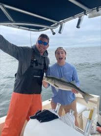 Two anglers celebrating a successful catch of a striped bass while fishing on a boat, showcasing their excitement on the water.