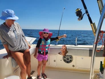 A young girl proudly displaying her catch, a colorful fish, while enjoying a day of fishing on a boat in open waters.
