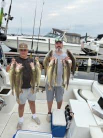 A young angler and an adult proudly displaying their catch of Walleye on a fishing charter, with boats visible in the background.