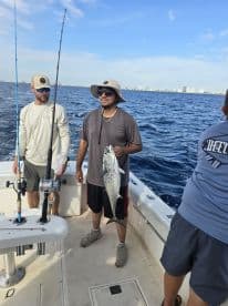 Two anglers aboard a boat, with one proudly displaying a large Spanish Mackerel caught during a deep-sea fishing trip.