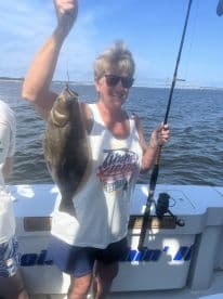 An enthusiastic angler proudly displaying a large Flounder while fishing on a boat, showcasing a sunny day on the water.