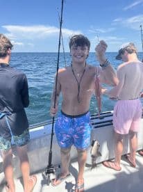 Young angler smiling while holding two fish, a Snapper and a Grouper, on a fishing charter in clear blue waters.