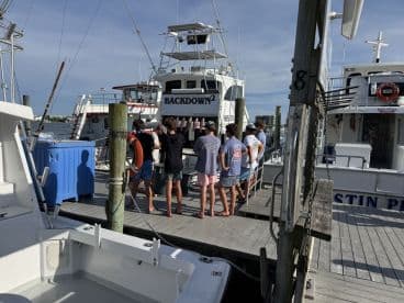 A group of anglers gathered at the dock, possibly discussing their fishing trip, with several boats visible in the background.