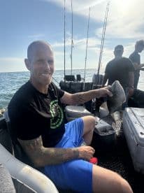 An angler proudly displaying a freshly caught fish while enjoying a day of fishing on a boat in open waters.