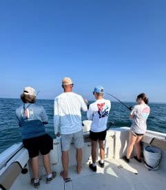 A group of anglers actively fishing from a boat, with one person reeling in a catch while others prepare their lines, enjoying a sunny day on the water.