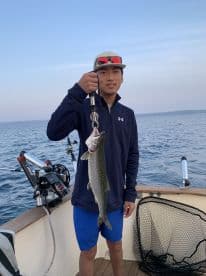 Young angler proudly holding a large Lake Trout while fishing on a boat, showcasing a successful catch in a scenic waterway.