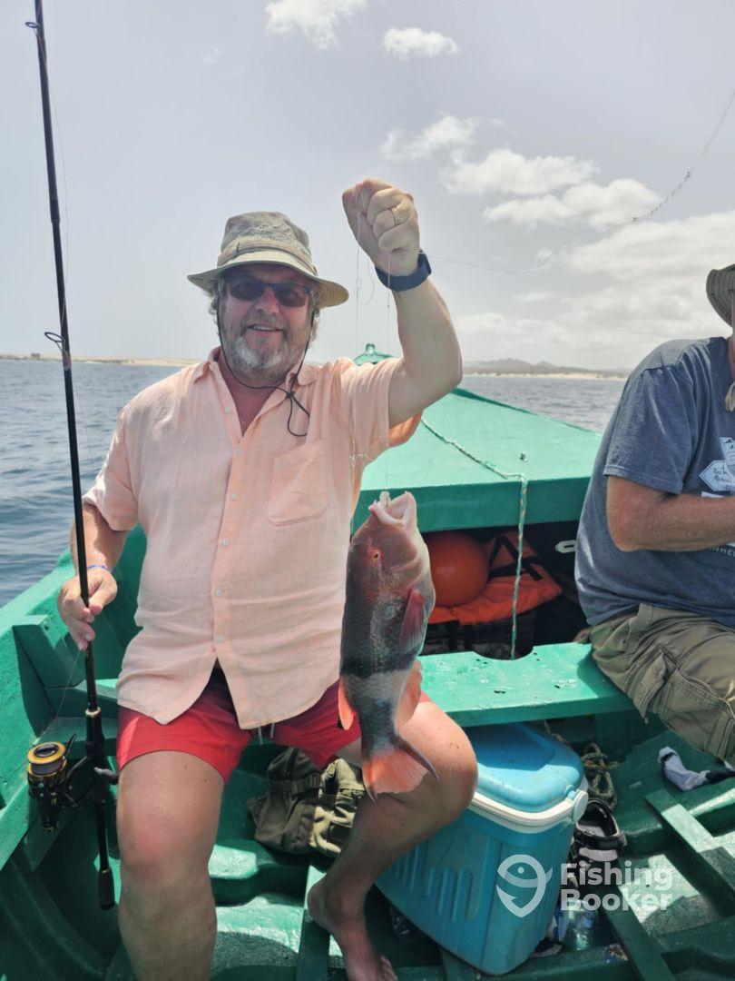 An angler proudly displaying a colorful Parrotfish while fishing from a small boat in a sunny coastal environment.