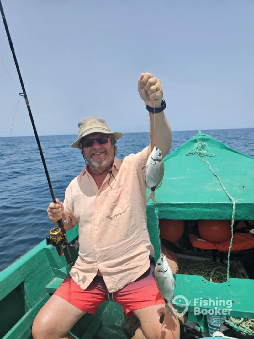 An angler proudly displaying his catch of two fish while fishing from a small green boat in open waters.