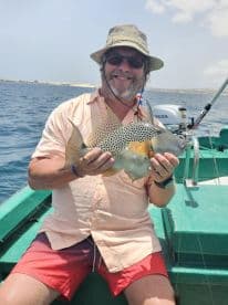 An angler proudly displaying a colorful fish while fishing from a small boat in clear waters, showcasing a successful day on the water.