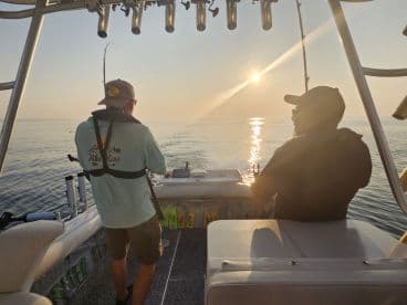 Two anglers engaged in fishing during sunrise on a boat, showcasing a tranquil ocean environment.