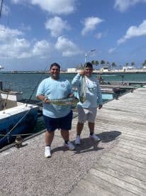 Two anglers proudly displaying their catch of Mahi Mahi at the dock, showcasing a successful day of fishing in a tropical setting.