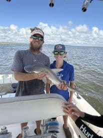 Two anglers proudly displaying a caught shark on a fishing boat, enjoying a day on the water.