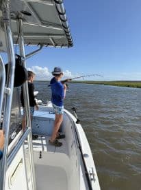 Two young anglers actively fishing from a boat in a scenic waterway, showcasing the excitement of the catch.