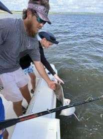A young angler and an adult are working together to reel in a stingray while fishing from a boat in a coastal waterway.