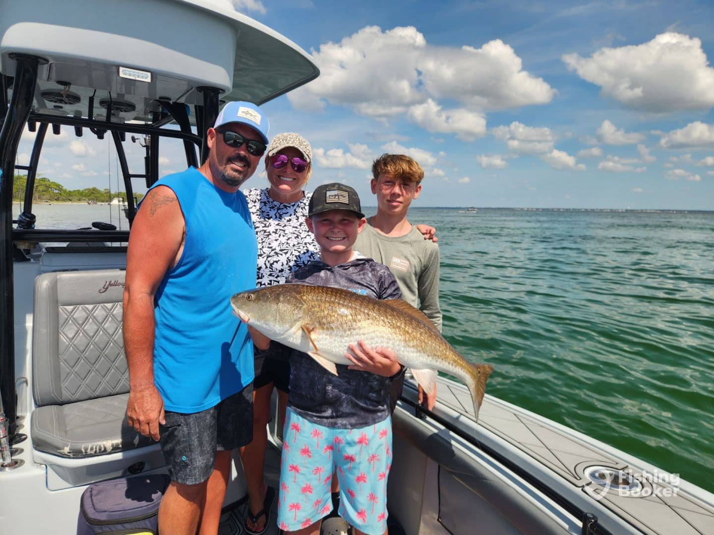 A family proudly displays a large Redfish on a boat during a sunny day on the water.