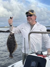 Angler proudly displaying a large Flounder while fishing from a boat in a coastal environment.