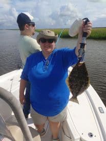 Angler proudly displaying a Flounder while fishing on a boat in a scenic coastal environment.