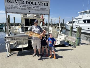 A proud family showcases a large Redfish caught during their fishing trip on the Silver Dollar III catamaran charter boat.