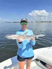 A young angler proudly displaying a caught shark while fishing on a sunny day, showcasing the excitement of a successful outing.