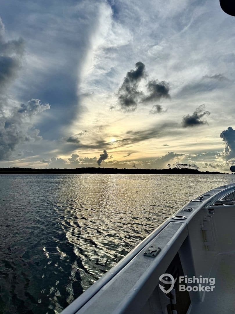 A scenic view of the boat's side against a vibrant sunset, reflecting on calm waters, showcasing the tranquil fishing environment.
