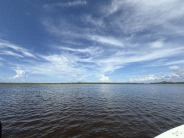 A scenic view of a calm river under a blue sky with scattered clouds, showcasing the tranquil fishing environment.