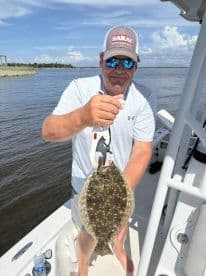 Angler proudly displaying a large Flounder while fishing from a boat in a calm waterway.