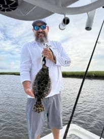 An angler proudly displaying a Flounder while fishing in a scenic coastal environment.