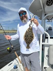 Angler proudly displaying a Flounder while fishing from a boat in a coastal waterway.