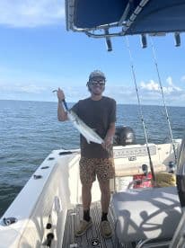 Angler proudly displaying a large Spanish Mackerel while aboard a center console boat in open waters.