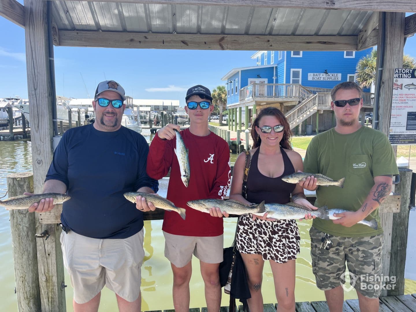 A group of four anglers proudly displaying their catch of Speckled Trout at the dock, showcasing a successful day of fishing.