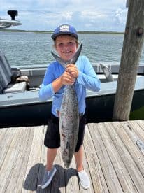 Young angler proudly holding a large King Mackerel at the dock after a Gulf Coast fishing trip.