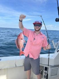 Angler proudly displaying a vibrant Red Snapper while fishing offshore, showcasing a successful day on the water.
