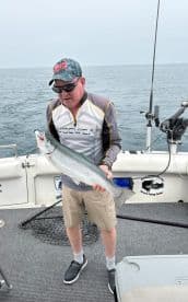 Angler holding a large Silver Salmon aboard a fishing boat in open waters, showcasing a successful catch.