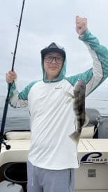 Young angler proudly displaying a caught fish while fishing on a boat, showcasing a calm day on the water.