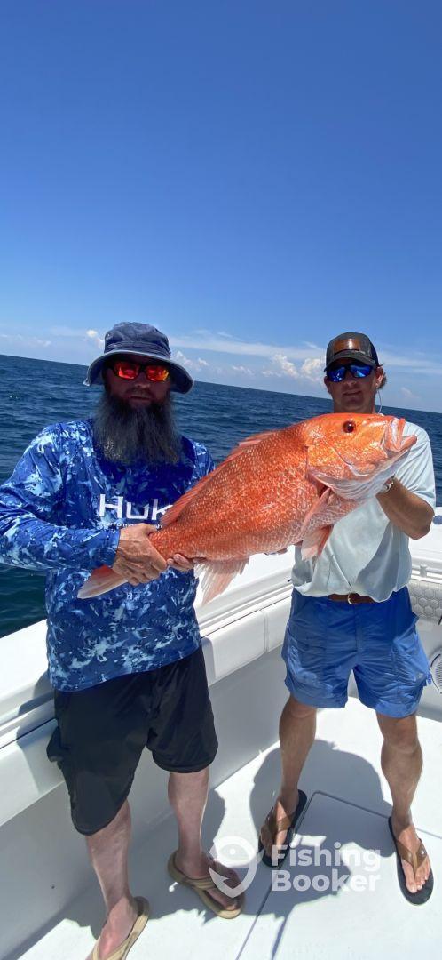 Two anglers proudly displaying a large Red Snapper while fishing offshore, showcasing a successful day on the water.