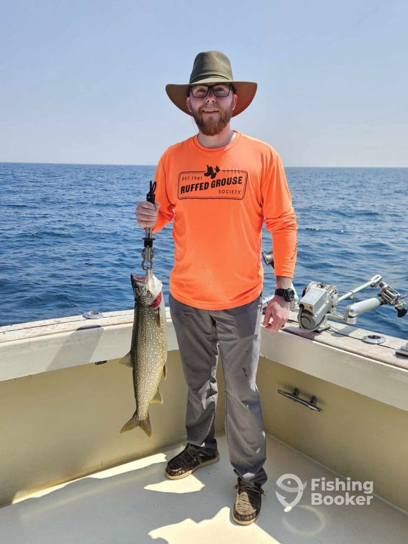 Angler proudly displaying a large Lake Trout while fishing on a boat in open waters.