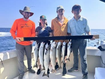 A group of four anglers proudly displaying their catch of multiple Lake Trout on a fishing charter in open waters.