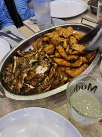 A platter of fried fish and seafood served at a dining table, with drinks and plates visible, suggesting a social dining experience.
