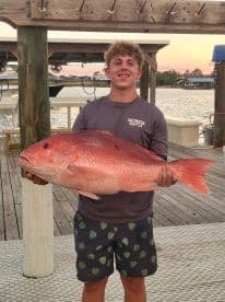 A young angler proudly displaying a large Red Snapper at the dock during a sunset fishing trip.